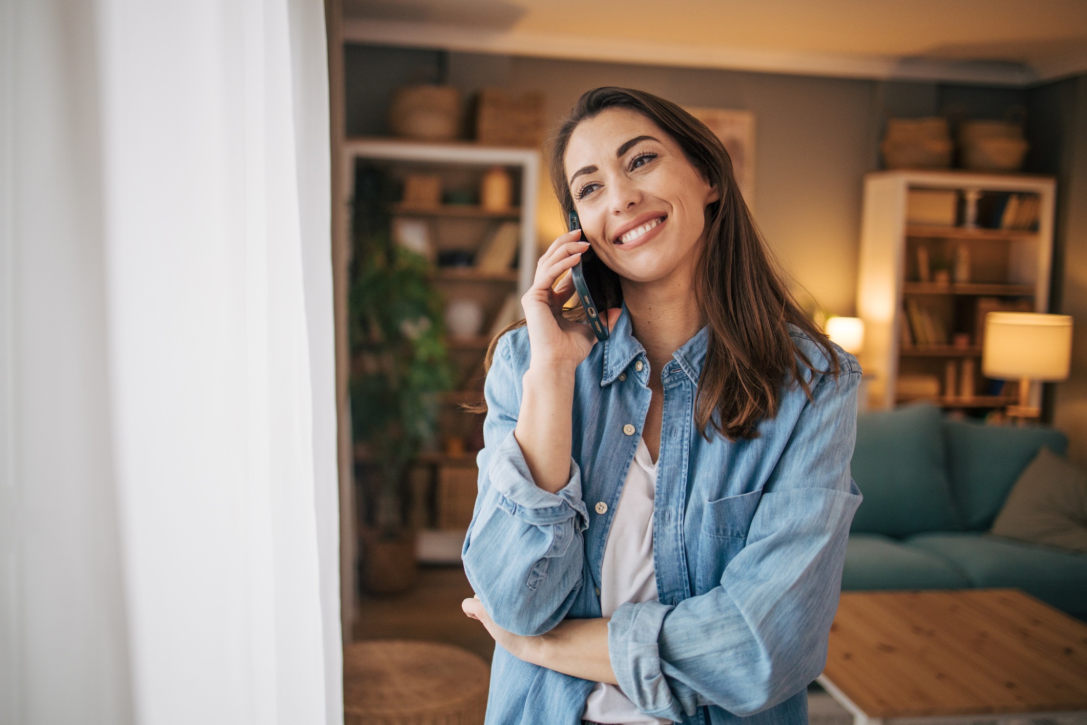 Photo of a woman have a phone call with friend while standing in livingroom